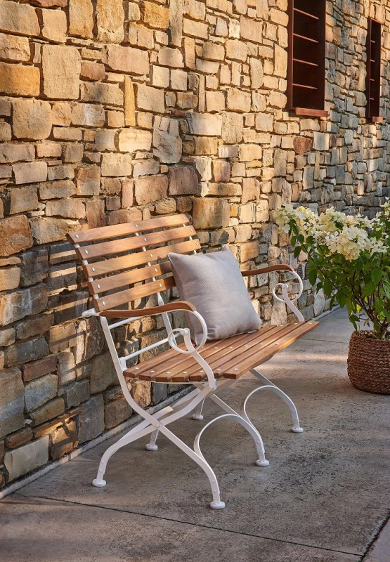 Schöne Parkbank aus Holz mit einem Gestell aus Metall in Weiß, vor einer Natursteinwand