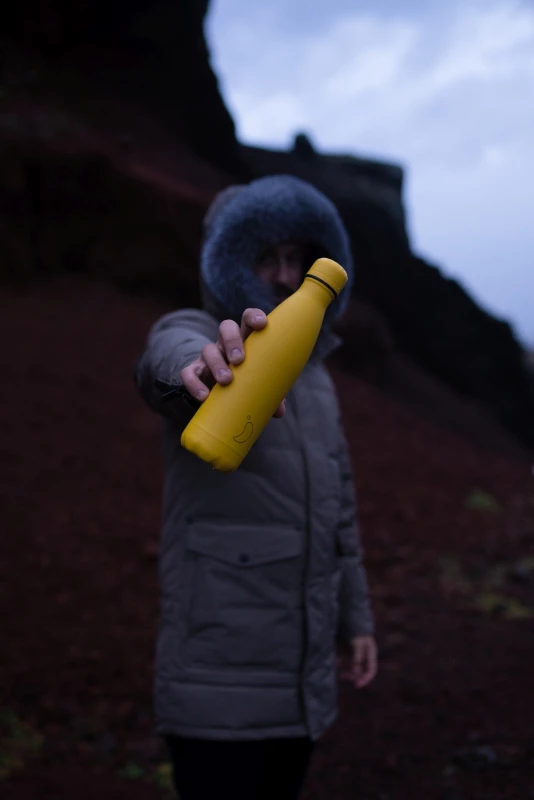 Ein Mann in einer dicken Winterjacke hält eine gelbe Chilly`s Trinkflasche vor sich gestreckt