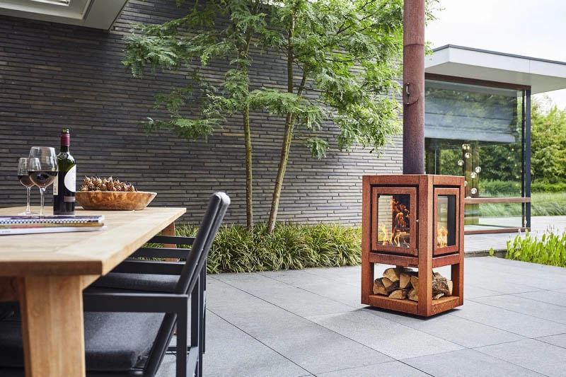 Gartenkamin von RB73 schön in Szene gesetzt auf einer stylischen Terrasse mit einem gedeckten Tisch im Vordergrund