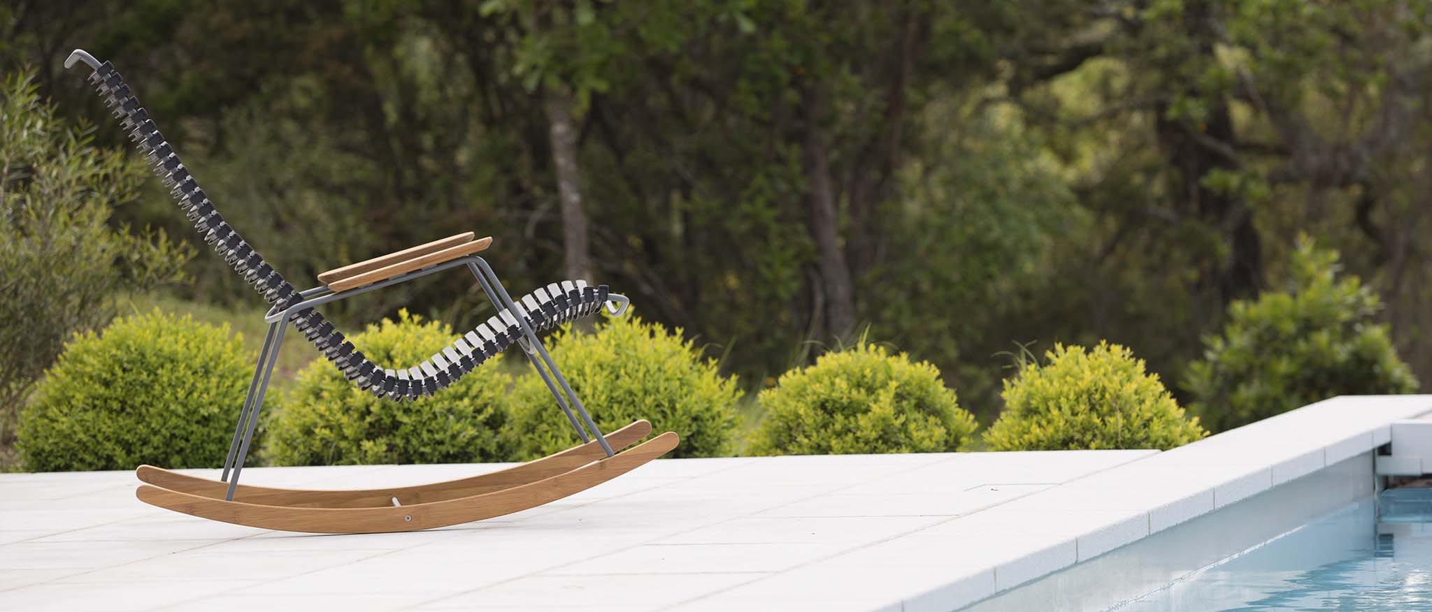 Moderner Schaukelstuhl mit Kufen aus Holz auf einer Terrasse vor einem Pool