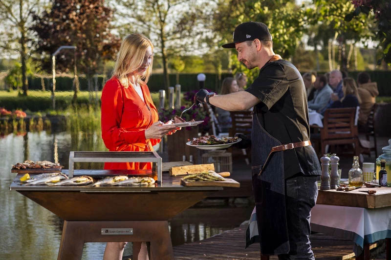 Quan Garden Art Ein Koch übergibt fertig gegrilltes Essen von einem Quan Garden Art Grill an eine Kundin