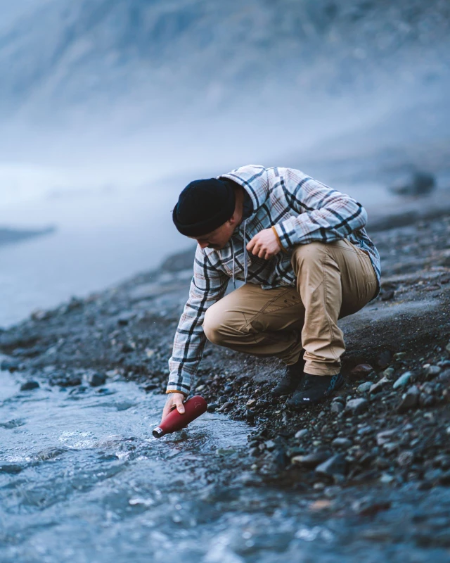 Ein Mann füllt seine rote Chilly`s Trinkflasche an einem Bach auf
