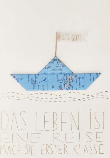 Grußkarte „Das Leben ist eine Reise“ – Karte mit Papierschiff und Flagge