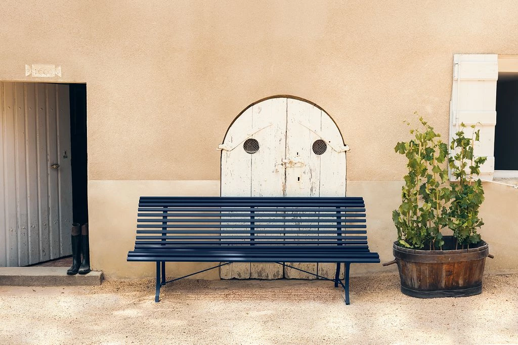 Premium Parkbank Outdoor Premium Parkbank Louisiane in blau vor einer beigen Hauswand neben einer Pflanze